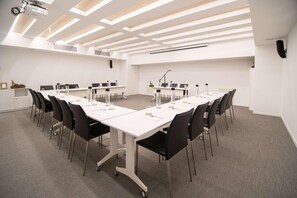 Een vergaderruimte met witte tafels, zwarte stoelen en een plafond met dakramen.