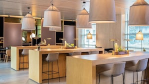 Zona de bar moderna con mostradores de madera, taburetes, iluminación colgante y vistas a la ciudad a través de grandes ventanales.