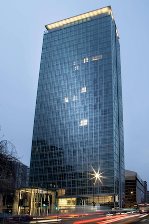 A tall glass building with a modern design, featuring a prominent entrance and a star-shaped light fixture. - Innside Milano Torre Galfa (Milan)