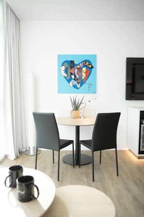 Un espace repas moderne avec une table ronde, deux chaises noires et un tableau abstrait bleu accroché au mur.