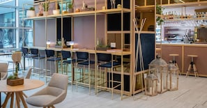 Zona de bar moderna con asientos, estanterías con plantas y una barra con vasos.