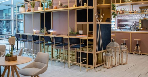Zona de bar moderna con asientos, estanterías con plantas y una barra con vasos.