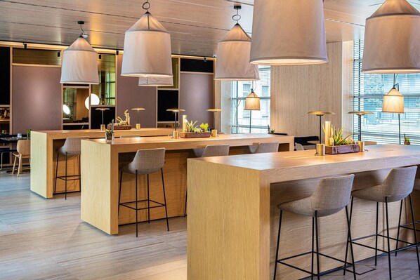 Zona de bar moderna con mostradores de madera, taburetes, iluminación colgante y vistas a la ciudad a través de grandes ventanales.