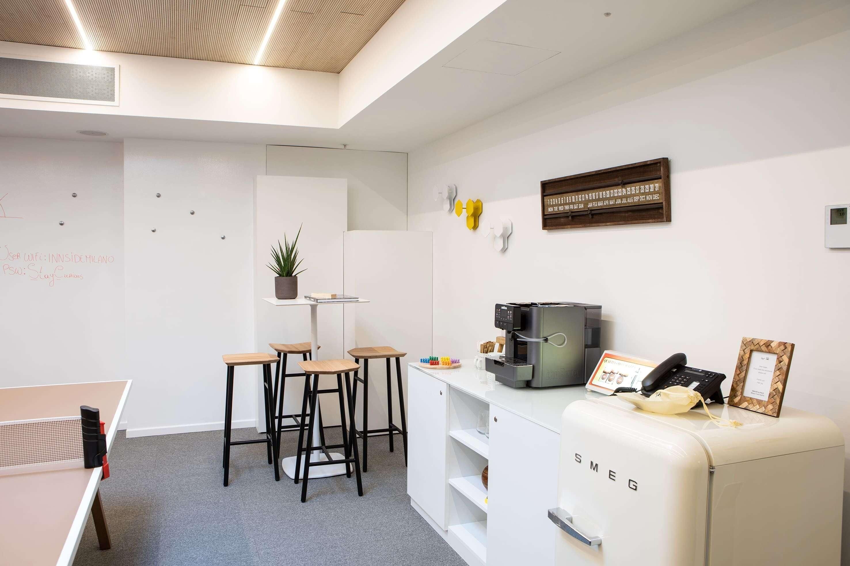 Un espacio de oficina moderno con mesa de ping pong, taburetes de bar, cafetera y refrigerador antiguo.