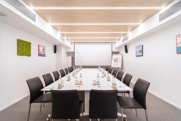 Un salón de conferencias con una larga mesa, sillas negras y una pantalla de proyector.