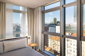 Une chambre d’hôtel moderne dotée de grandes fenêtres, d’un lit et d’une table de chevet.