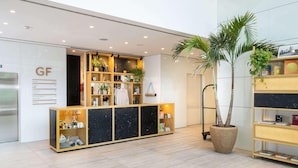 Un área de recepción con mostrador de madera, plantas en macetas y un cartel que indica la disponibilidad de habitaciones.