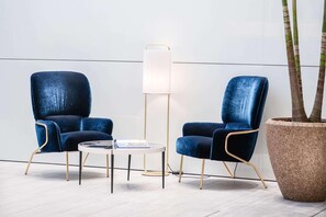 Una habitación moderna con dos sillones de terciopelo azul, una lámpara de pie blanca y una mesa de centro redonda.