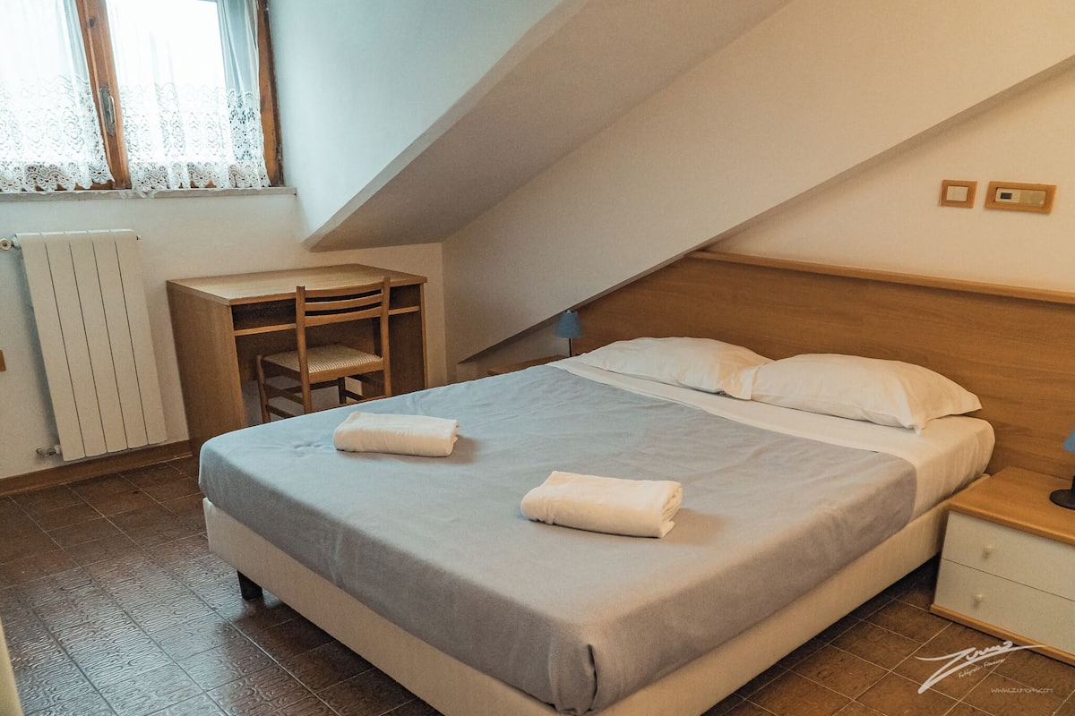 A bedroom with a bed, two bedside tables, a desk, and a chair.