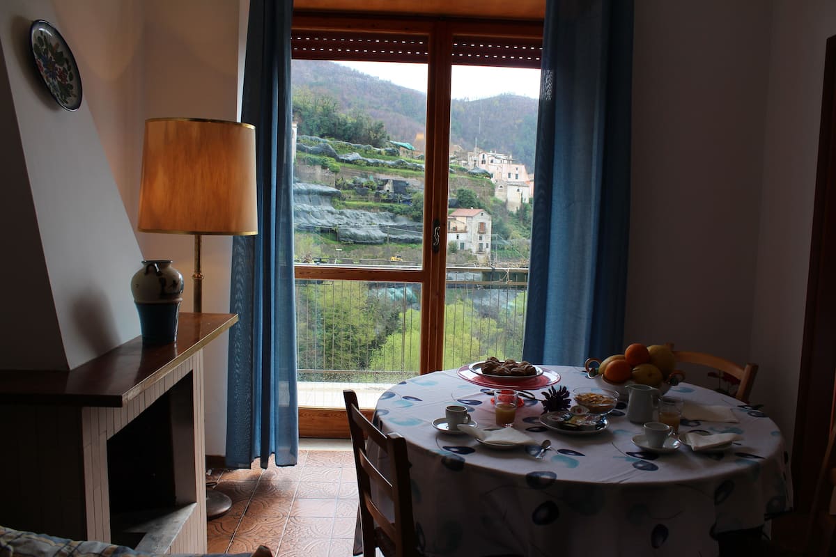 A dining area with a table set for breakfast, a view of terraced fields, and a wooden door.