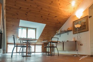 A dining area with a wooden ceiling, a table with chairs, a window, and a wall-mounted shelf with decorative items.