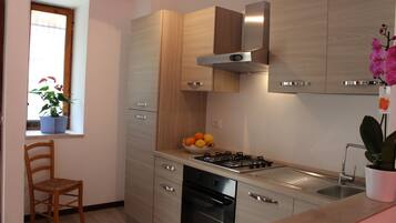 A modern kitchen with wooden cabinets, a gas stove, a black dishwasher, and a window with a potted plant.