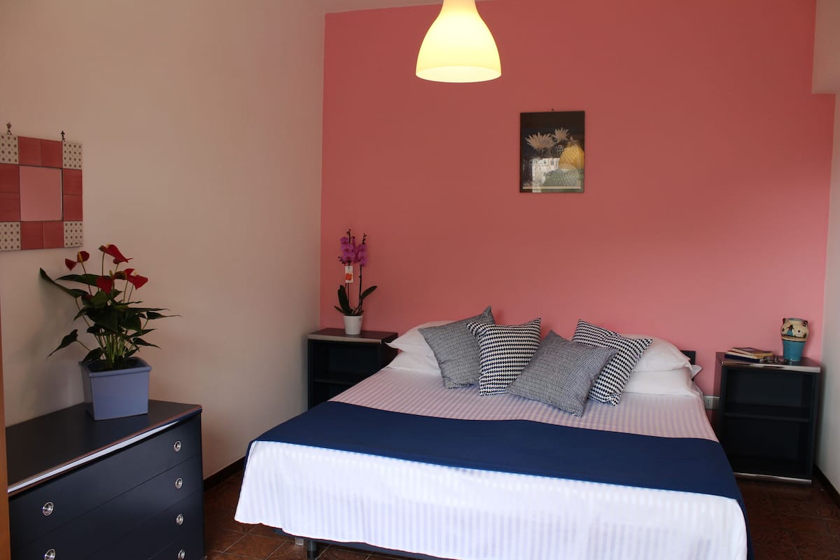 A bedroom with a bed, two nightstands, a dresser, a wall-mounted light fixture, and a framed picture.