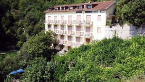 Un edificio de varios pisos con balcones, rodeado de abundante vegetación.
