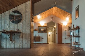 A spacious lobby with a wooden ceiling, a stone wall with a circular artwork, and a reception desk. - Tramonti Green (Tramonti)