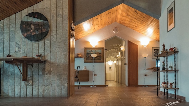 Un vestíbulo amplio con techo de madera, pared de piedra y una obra de arte circular, junto a un mostrador de recepción.