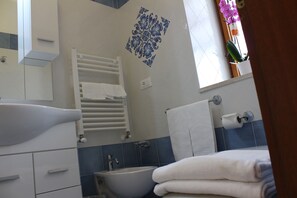 A bathroom with a white sink, a towel rack, a decorative tile wall, and a window with a plant.