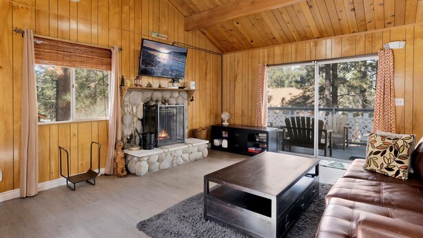 Ein gemütliches Blockhaus-Interieur mit Kamin aus Stein, Holzwänden, einem darüber montierten Fernseher und einer komfortablen Sitzecke mit Sofa und Couchtisch.