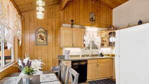 Ein Holzinterieur mit einem für zwei Personen gedecktem Esstisch, einer Küche mit Holzschränken und einem Schild mit der Aufschrift 'Sie fangen und putzen, wir kochen und essen'.
