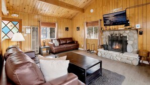 Ein gemütliches Blockhaus-Interieur mit Kamin aus Stein, Ledersofa und Fernseher, der über dem Kamin angebracht ist.