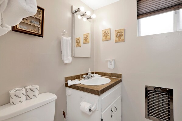 A bathroom with a toilet, sink, mirror, and towel rack. - Sweet Cabin Home Gateway #2576 (Big Bear City)