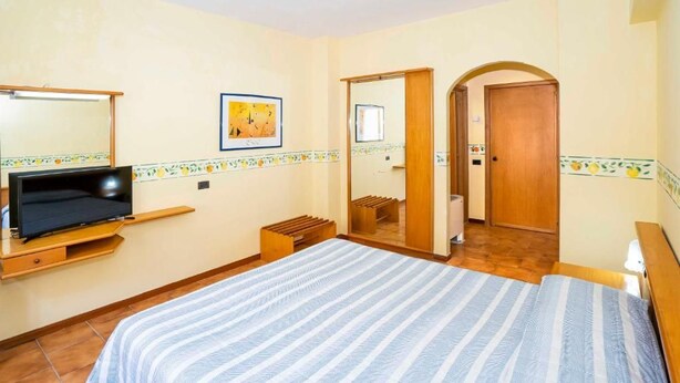 A bedroom with a bed, a TV on a stand, a mirror, and a door leading to another room. - Hotel San Pietro Beach - Letojanni (Letojanni)