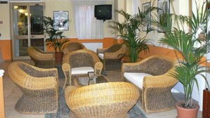 A lobby with wicker furniture, potted plants, a television, and a glass door entrance.