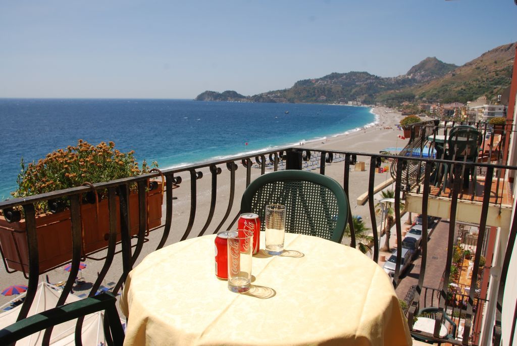 A balcony with a table, chairs, and a view of the sea and a beach.