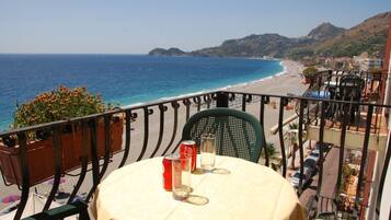 Uma varanda com mesa, cadeiras e vista para o mar e a praia.