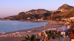 A beach with a view of a hillside town, a pier, and a row of beachside buildings. - Hotel San Pietro Beach - Letojanni (Letojanni)