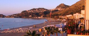 A beach with a view of a hillside town, a pier, and a row of beachside buildings. - Hotel San Pietro Beach - Letojanni (Letojanni)