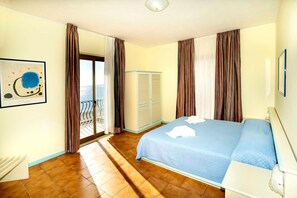 A bedroom with a bed, a window with curtains, a door leading to a balcony, and a wall-mounted artwork. - San Pietro Beach (Letojanni)
