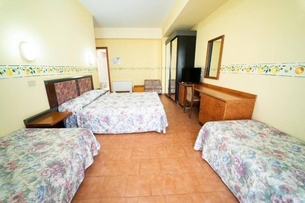 A hotel room with two single beds, a desk with a chair, a television, and a mirror on the wall.