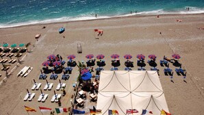 A beach with rows of sun loungers and umbrellas, a tent, and flags.