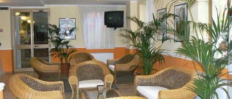 A lobby with wicker furniture, potted plants, a television, and a glass door entrance.