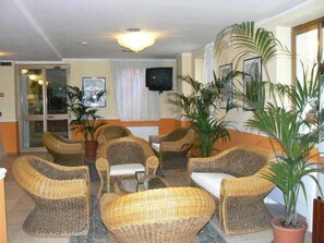A lobby with wicker furniture, potted plants, a television, and a glass door entrance. - Hotel San Pietro Beach - Letojanni (Letojanni)