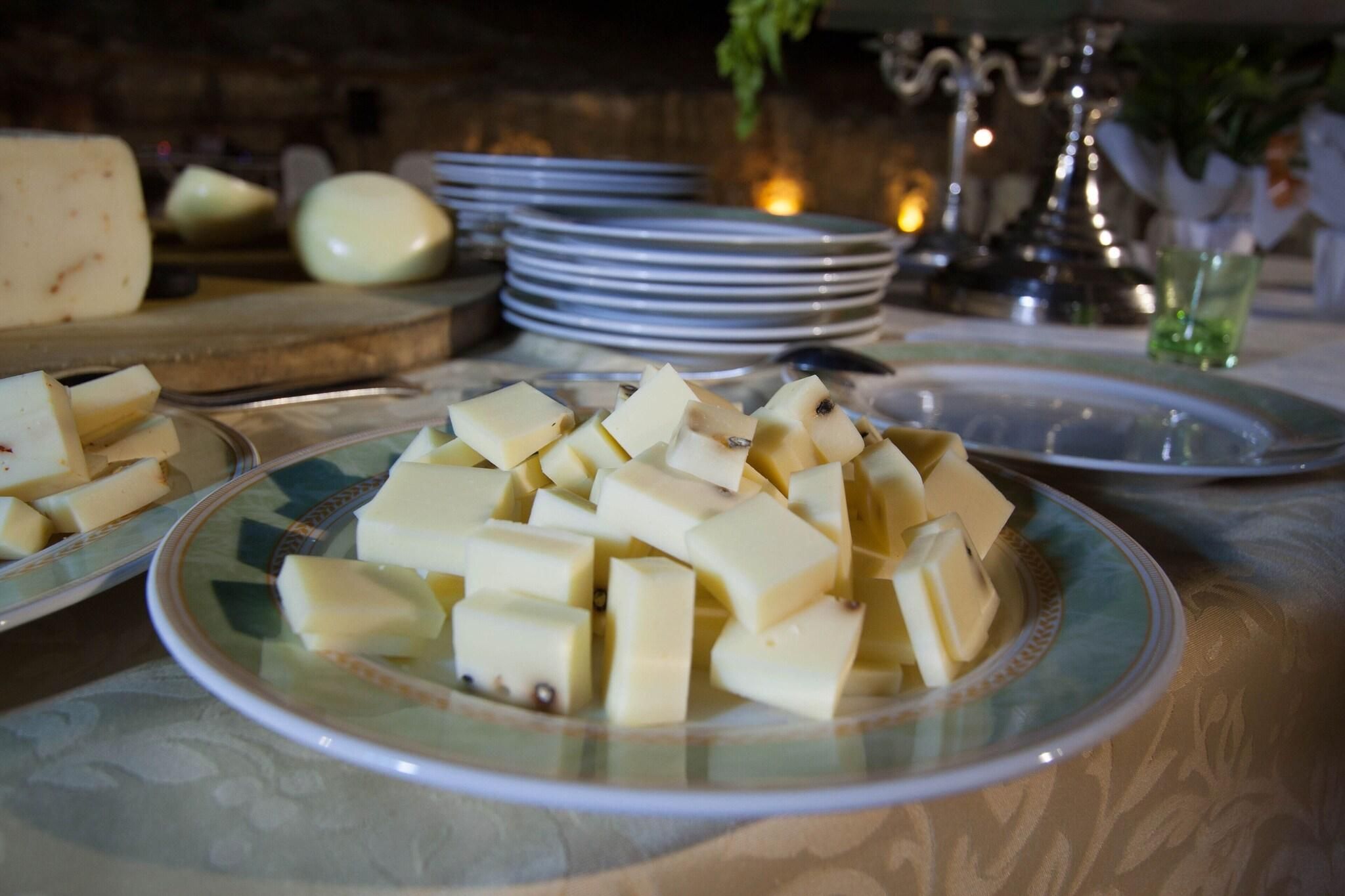 Una mesa con platos de queso en cubos, una tabla de cortar con queso y platos apilados al fondo.