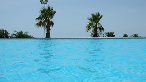 Una piscina con agua cristalina azul, rodeada de palmeras y un cielo despejado.