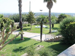 A landscaped garden with palm trees, a paved pathway, and white chairs. - Villa Principe Di Belmonte (Modica)