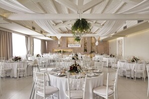 A banquet hall with round tables set for a formal event, featuring white tablecloths and chairs, a chandelier, and a sign reading "Principe di Vellemonde". - Villa Principe Di Belmonte (Modica)