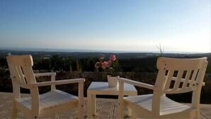 Dos sillas blancas con una mesa pequeña y un florero, con vistas a un paisaje pintoresco.