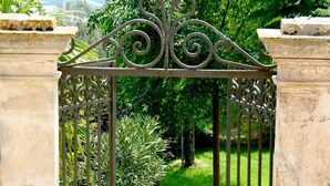 Una ornamentada puerta de hierro forjado que da acceso a un exuberante jardín con vistas a colinas distantes.