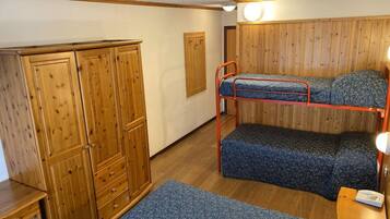 Un letto a castello con materasso decorato, un armadio in legno e un tavolino con una lampada.