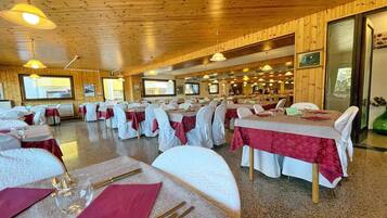 Un ristorante con diversi tavoli apparecchiati, soffitto in legno e vista sull'area della cucina.