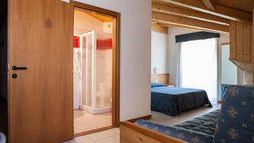 Una stanza con una porta in legno che dà su un bagno, un letto con copriletto blu e una finestra vista esterna.