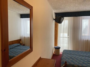 A bedroom with a bed, a nightstand, a mirror, a window with curtains, and a wall-mounted lamp. - Hotel Union (Dimaro Folgarida)