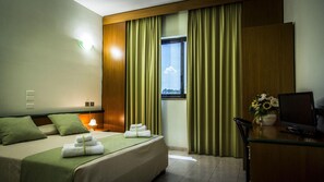 A hotel room with a bed, a desk, a chair, a TV, a window with curtains, and a view of the sky. - Hotel Cristallo Relais Sure Hotel Collection by Be (Tivoli)