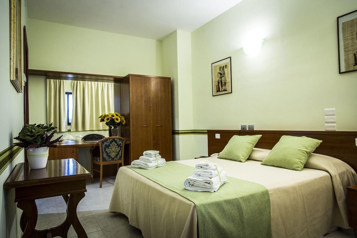 Een hotelkamer met een bed, bureau, stoel, kledingkast en spiegel.