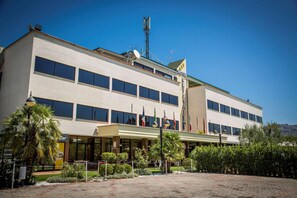 A modern hotel with a flat roof, multiple windows, and flags. - Hotel Cristallo Relais Sure Hotel Collection by Be (Tivoli)