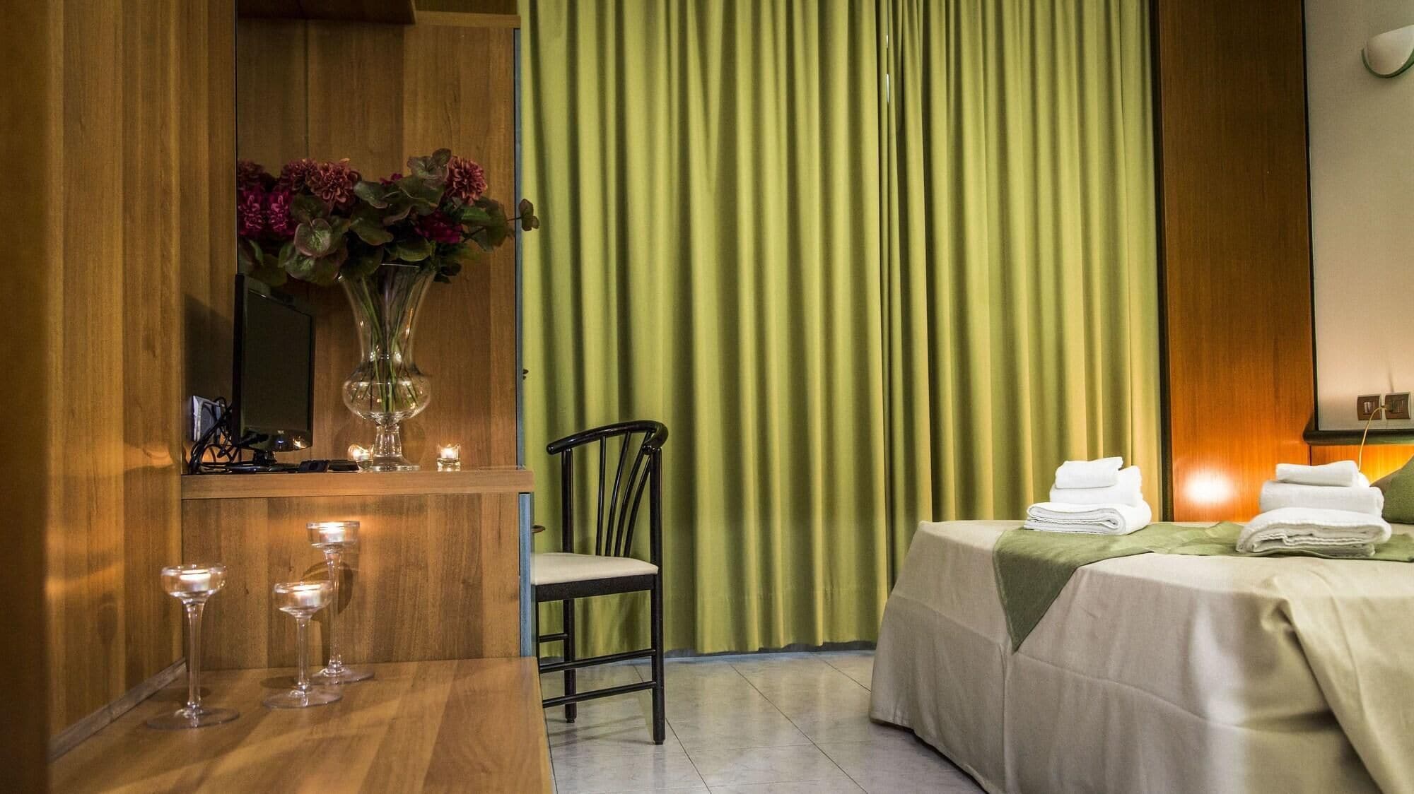 Hotelkamer met een houten bureau, een stoel, een bed met een groene dekbedovertrek en een gordijn op de achtergrond.